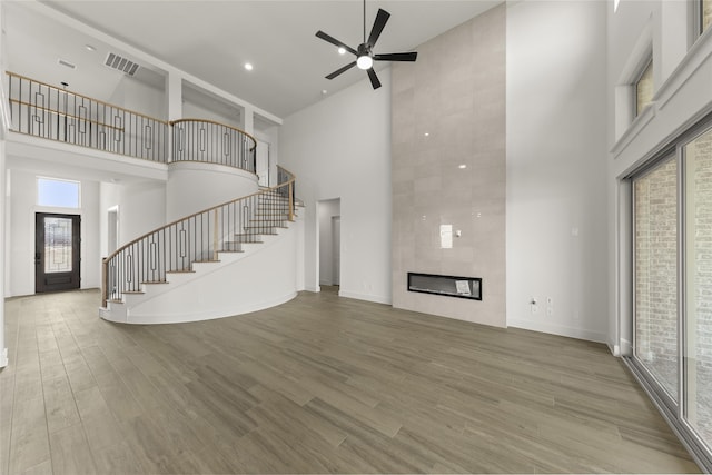 unfurnished living room featuring hardwood / wood-style floors, a towering ceiling, a tiled fireplace, and ceiling fan