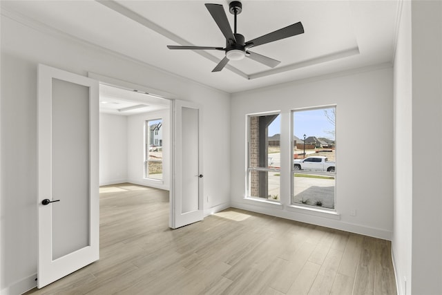 unfurnished room featuring ceiling fan, a tray ceiling, a healthy amount of sunlight, and light hardwood / wood-style flooring