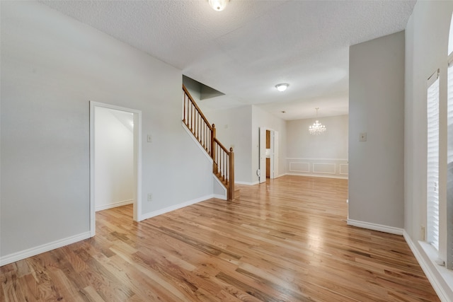 unfurnished room featuring light wood-type flooring, an inviting chandelier, and a textured ceiling