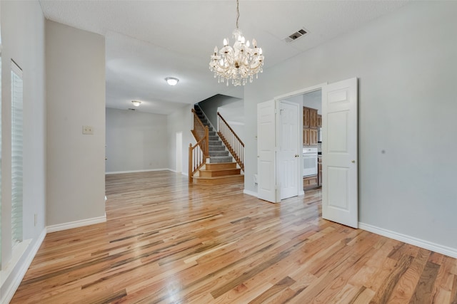 unfurnished dining area with light wood-type flooring, an inviting chandelier, and a textured ceiling