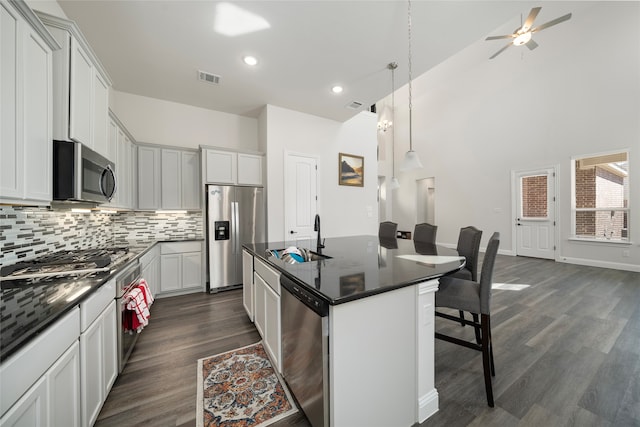 kitchen featuring appliances with stainless steel finishes, an island with sink, a breakfast bar, dark hardwood / wood-style flooring, and pendant lighting