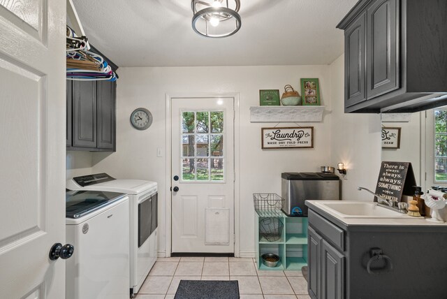 clothes washing area featuring light tile patterned floors, cabinets, washing machine and clothes dryer, and sink