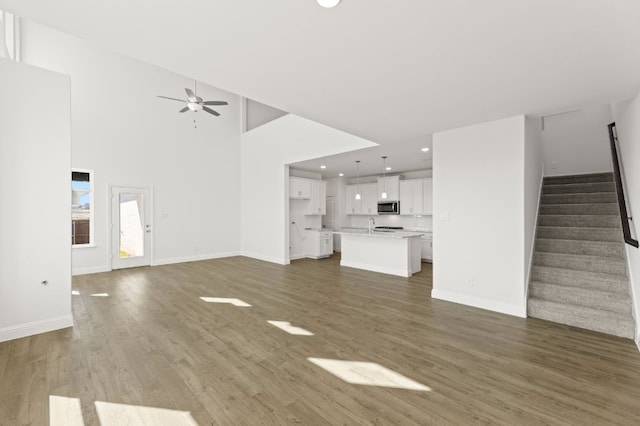 unfurnished living room with ceiling fan, dark hardwood / wood-style flooring, and a towering ceiling