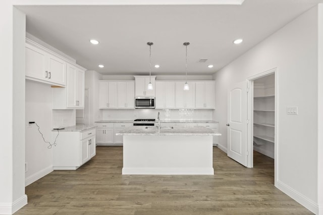 kitchen with hanging light fixtures, white cabinets, an island with sink, and light stone counters