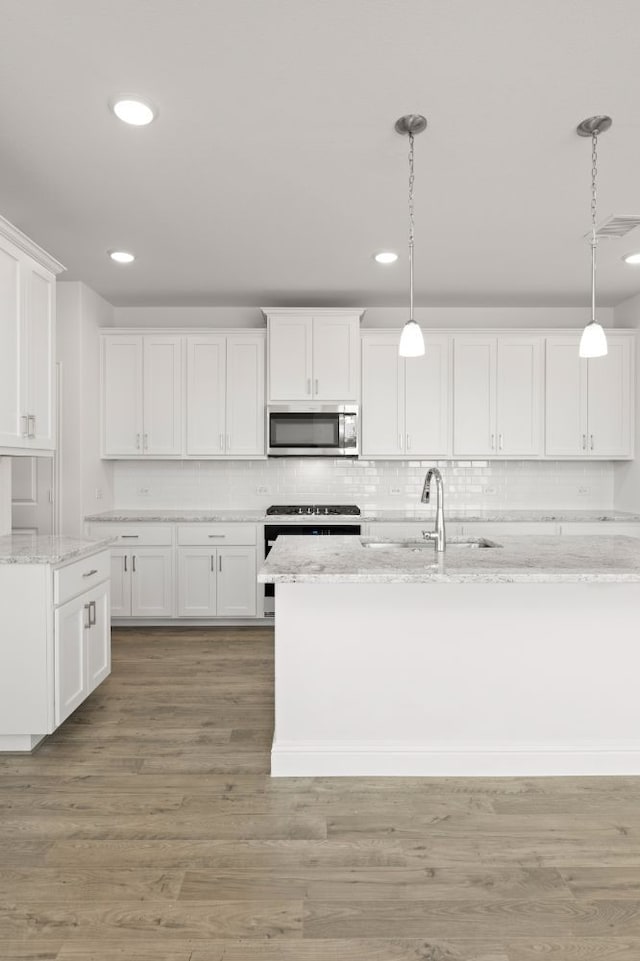 kitchen featuring light stone countertops, pendant lighting, white cabinets, appliances with stainless steel finishes, and hardwood / wood-style flooring