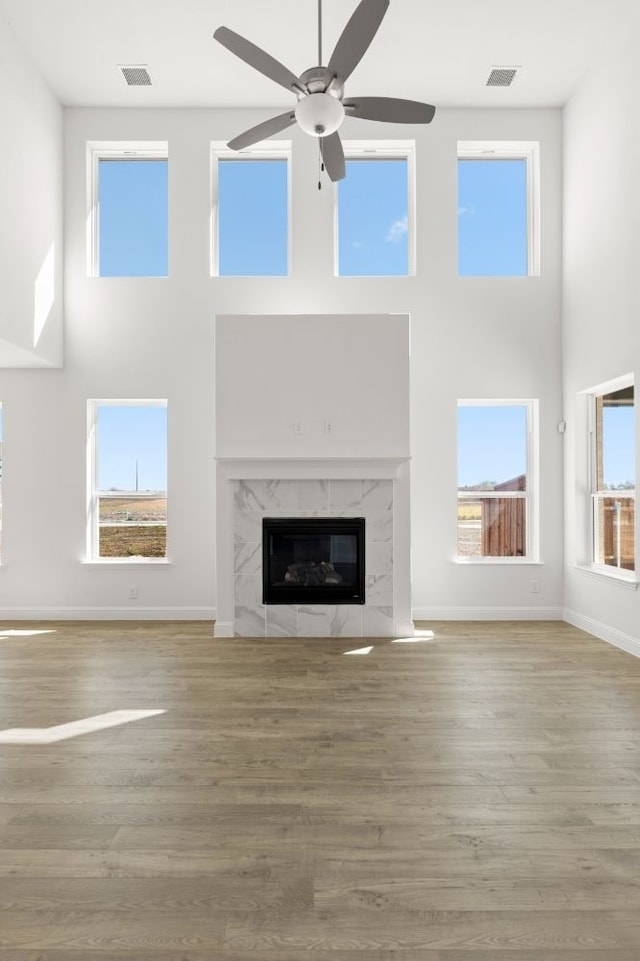 unfurnished living room featuring ceiling fan, a high ceiling, hardwood / wood-style floors, and a high end fireplace