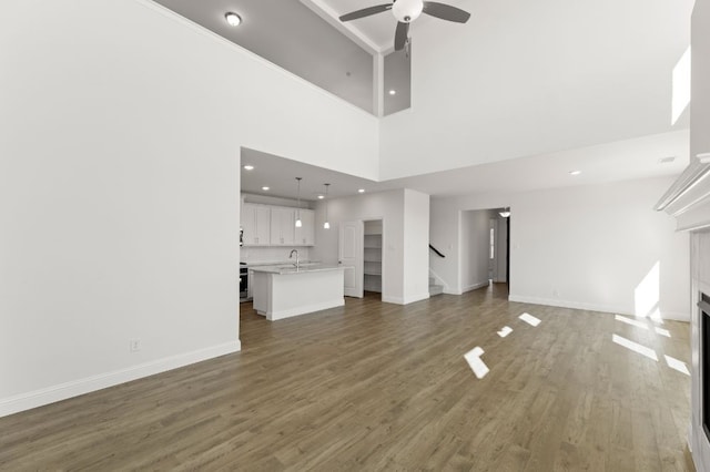 unfurnished living room with ceiling fan, dark hardwood / wood-style flooring, a high ceiling, and sink