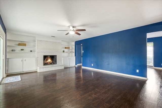 unfurnished living room featuring ceiling fan, dark wood-type flooring, built in shelves, and a fireplace