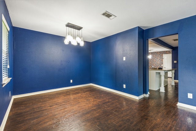 spare room with dark wood-type flooring and an inviting chandelier