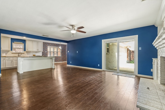 unfurnished living room with dark wood-type flooring, a brick fireplace, ceiling fan, and sink