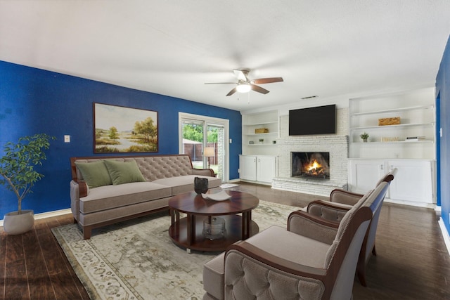 living room with ceiling fan, built in features, a brick fireplace, and dark hardwood / wood-style floors