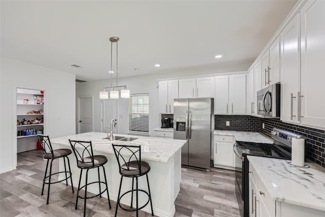 kitchen featuring hanging light fixtures, white cabinetry, a kitchen island with sink, and appliances with stainless steel finishes