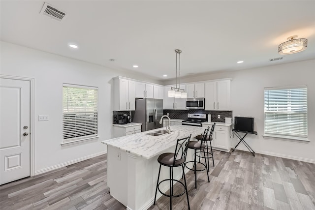 kitchen with sink, stainless steel appliances, pendant lighting, a center island with sink, and white cabinets