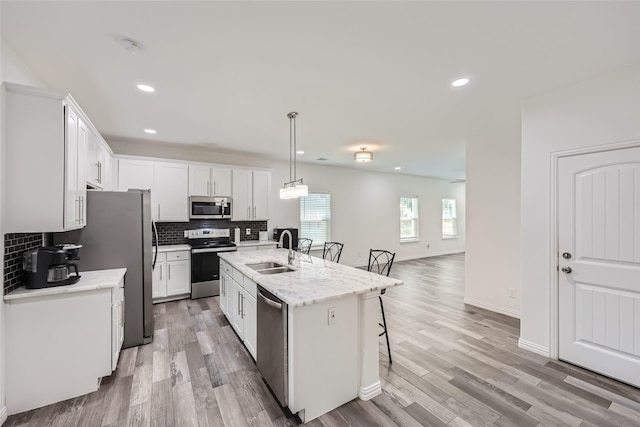 kitchen featuring appliances with stainless steel finishes, a kitchen island with sink, sink, pendant lighting, and white cabinetry