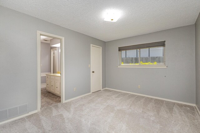 unfurnished bedroom featuring light carpet, a textured ceiling, a closet, and connected bathroom