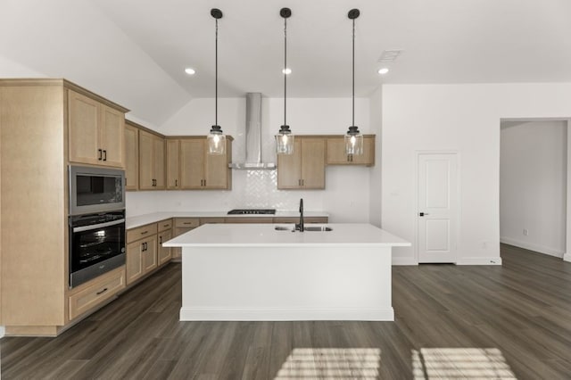 kitchen featuring a center island with sink, appliances with stainless steel finishes, hanging light fixtures, wall chimney exhaust hood, and sink