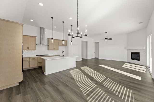 kitchen featuring a center island with sink, light brown cabinets, black gas stovetop, wall chimney range hood, and ceiling fan with notable chandelier