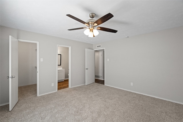 unfurnished bedroom featuring connected bathroom, ceiling fan, carpet, and a spacious closet