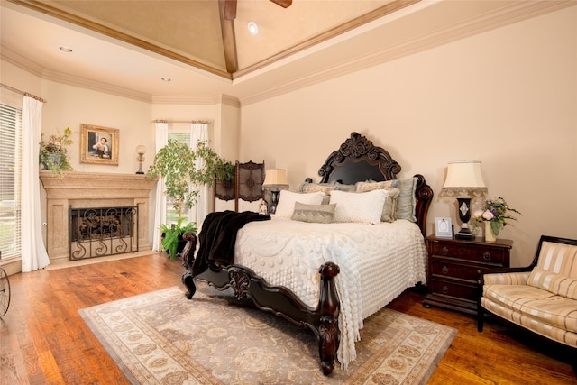 bedroom with ornamental molding, vaulted ceiling, ceiling fan, a premium fireplace, and hardwood / wood-style floors