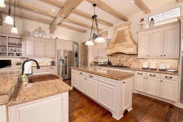 kitchen featuring pendant lighting, a kitchen island with sink, appliances with stainless steel finishes, beam ceiling, and custom range hood