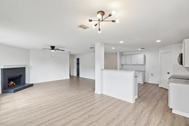 interior space with light wood-type flooring, ceiling fan with notable chandelier, a textured ceiling, and a brick fireplace