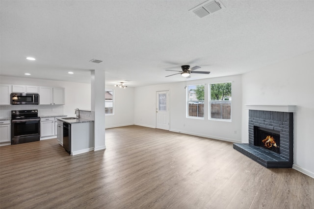 kitchen with sink, white cabinetry, a brick fireplace, black appliances, and hardwood / wood-style floors