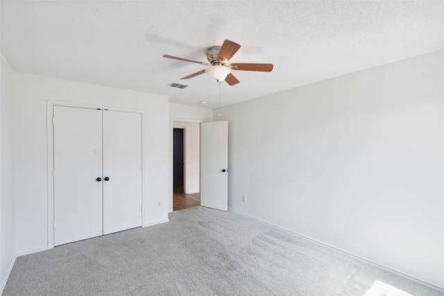 unfurnished bedroom with a textured ceiling, ceiling fan, light colored carpet, and a closet