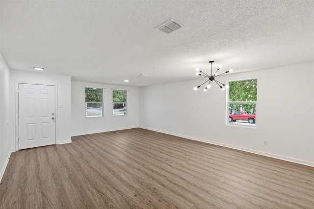 spare room with a textured ceiling, a chandelier, and hardwood / wood-style flooring