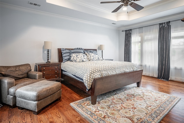 bedroom with hardwood / wood-style floors, ceiling fan, a raised ceiling, and ornamental molding