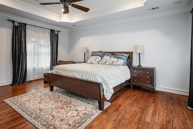 bedroom with ornamental molding, dark wood-type flooring, a tray ceiling, and ceiling fan