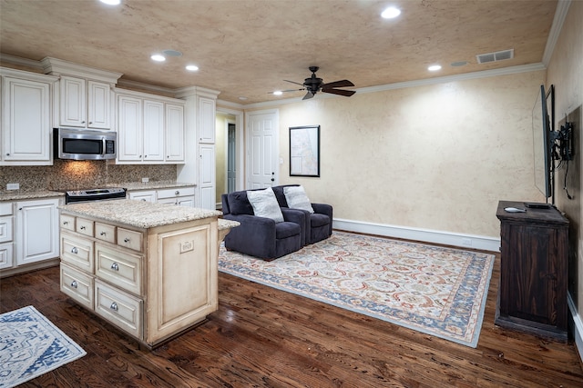 kitchen with appliances with stainless steel finishes, crown molding, dark wood-type flooring, a center island, and ceiling fan