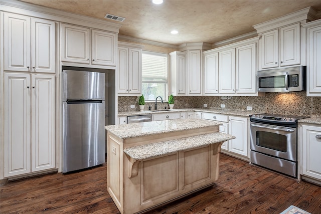 kitchen featuring dark wood-type flooring, appliances with stainless steel finishes, a kitchen island, and light stone countertops