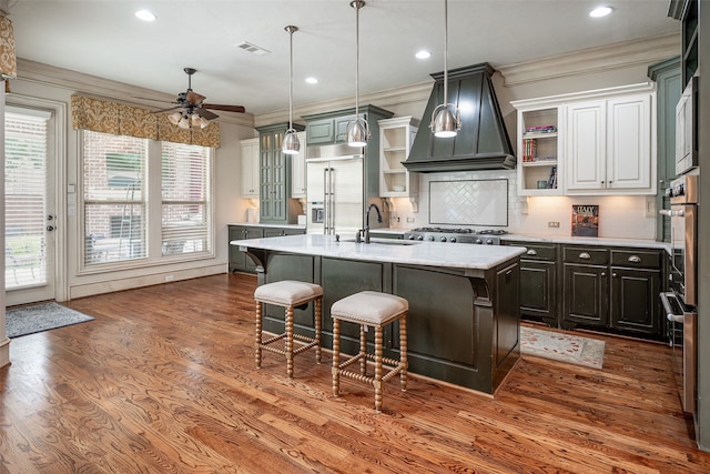 kitchen featuring white cabinetry, stainless steel appliances, premium range hood, ceiling fan, and a center island with sink