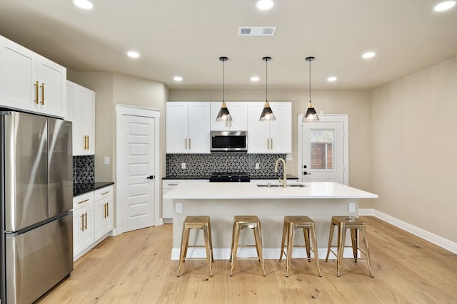 kitchen with visible vents, an island with sink, appliances with stainless steel finishes, decorative light fixtures, and a sink