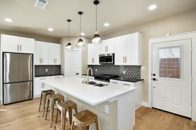 kitchen with stainless steel appliances, a sink, decorative light fixtures, and white cabinets