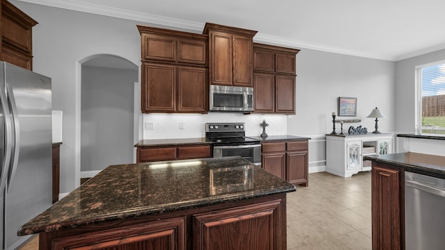 kitchen featuring dark stone countertops, a kitchen island, ornamental molding, and appliances with stainless steel finishes