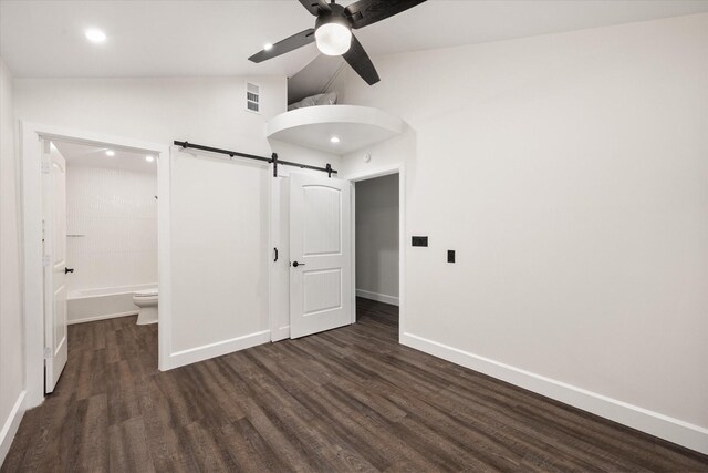 unfurnished bedroom featuring high vaulted ceiling, ceiling fan, dark wood-type flooring, ensuite bathroom, and a barn door