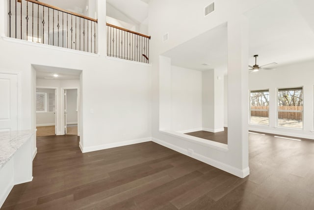 interior space with a towering ceiling, ceiling fan, and dark hardwood / wood-style floors