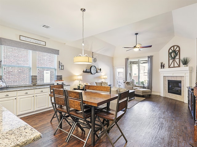 dining room with lofted ceiling, ceiling fan, a tile fireplace, and dark wood-type flooring