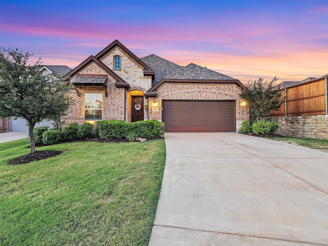 french country inspired facade featuring driveway, fence, a front yard, a garage, and brick siding