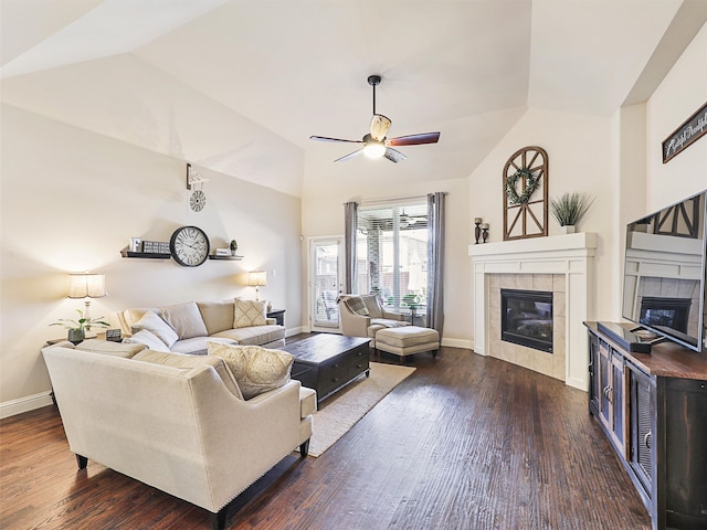 living room with ceiling fan, vaulted ceiling, a tiled fireplace, and dark wood-type flooring