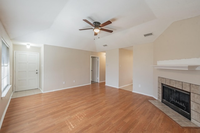 unfurnished living room with a tiled fireplace, lofted ceiling, ceiling fan, and light wood-type flooring