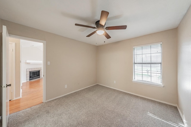 carpeted spare room with ceiling fan and a fireplace