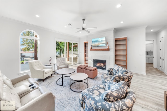 living room with a fireplace, crown molding, sink, ceiling fan, and light hardwood / wood-style floors