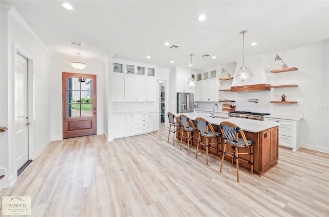 kitchen with light wood-type flooring, appliances with stainless steel finishes, white cabinetry, sink, and a center island with sink