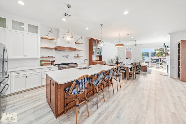 kitchen with white cabinets, decorative light fixtures, light hardwood / wood-style floors, sink, and a center island with sink