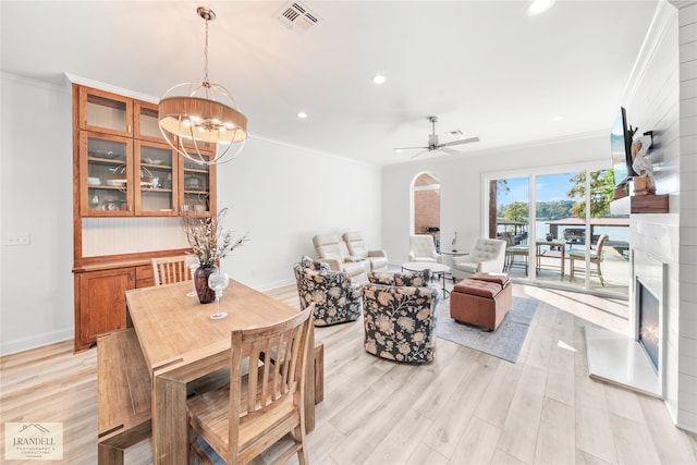 interior space featuring a large fireplace, ceiling fan with notable chandelier, ornamental molding, and light hardwood / wood-style flooring