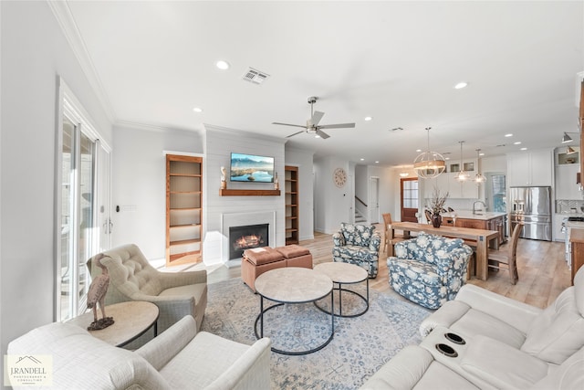 living room with a fireplace, light hardwood / wood-style flooring, sink, ceiling fan, and ornamental molding