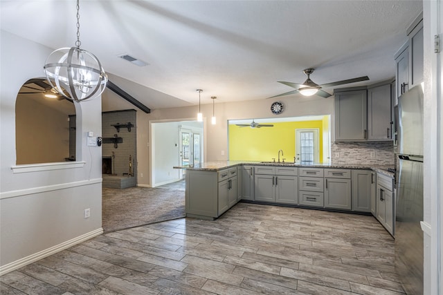 kitchen with gray cabinetry, light wood-type flooring, ceiling fan with notable chandelier, plenty of natural light, and kitchen peninsula