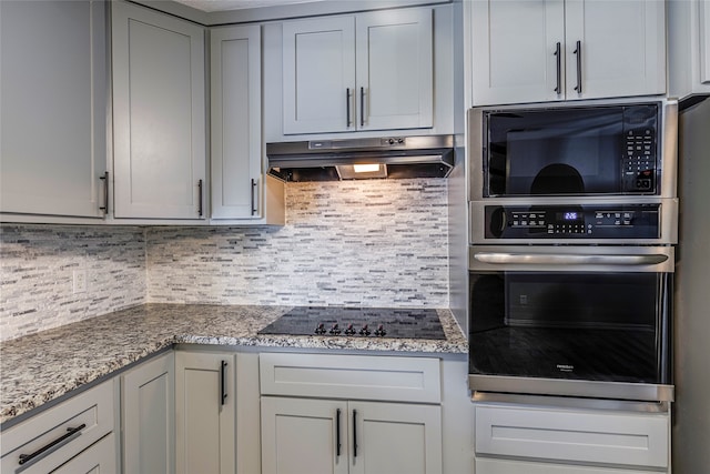 kitchen with black appliances, gray cabinets, light stone countertops, and decorative backsplash